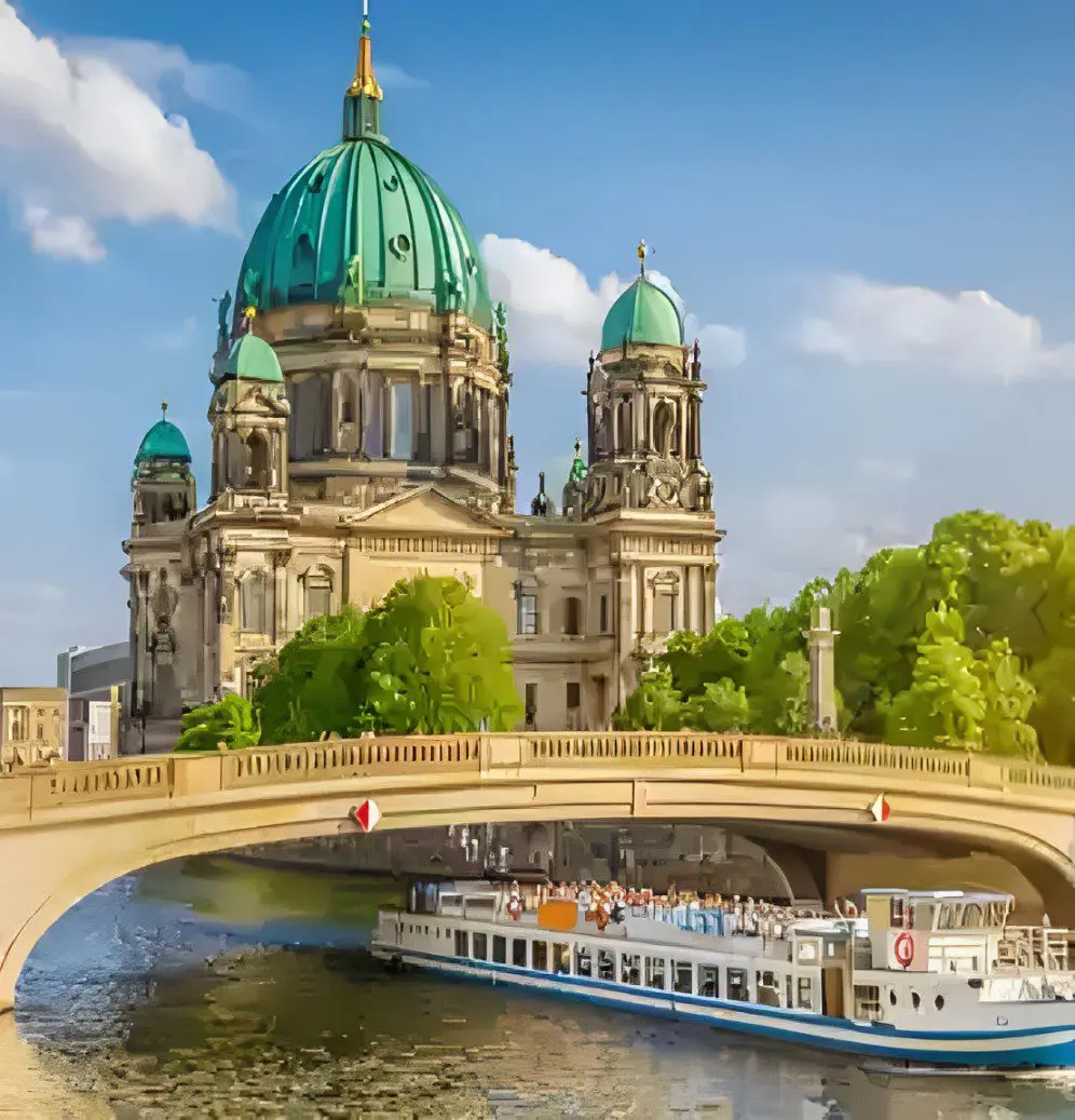 A white tour boat passes under a bridge near a large historic building with green domes and ornate architecture.