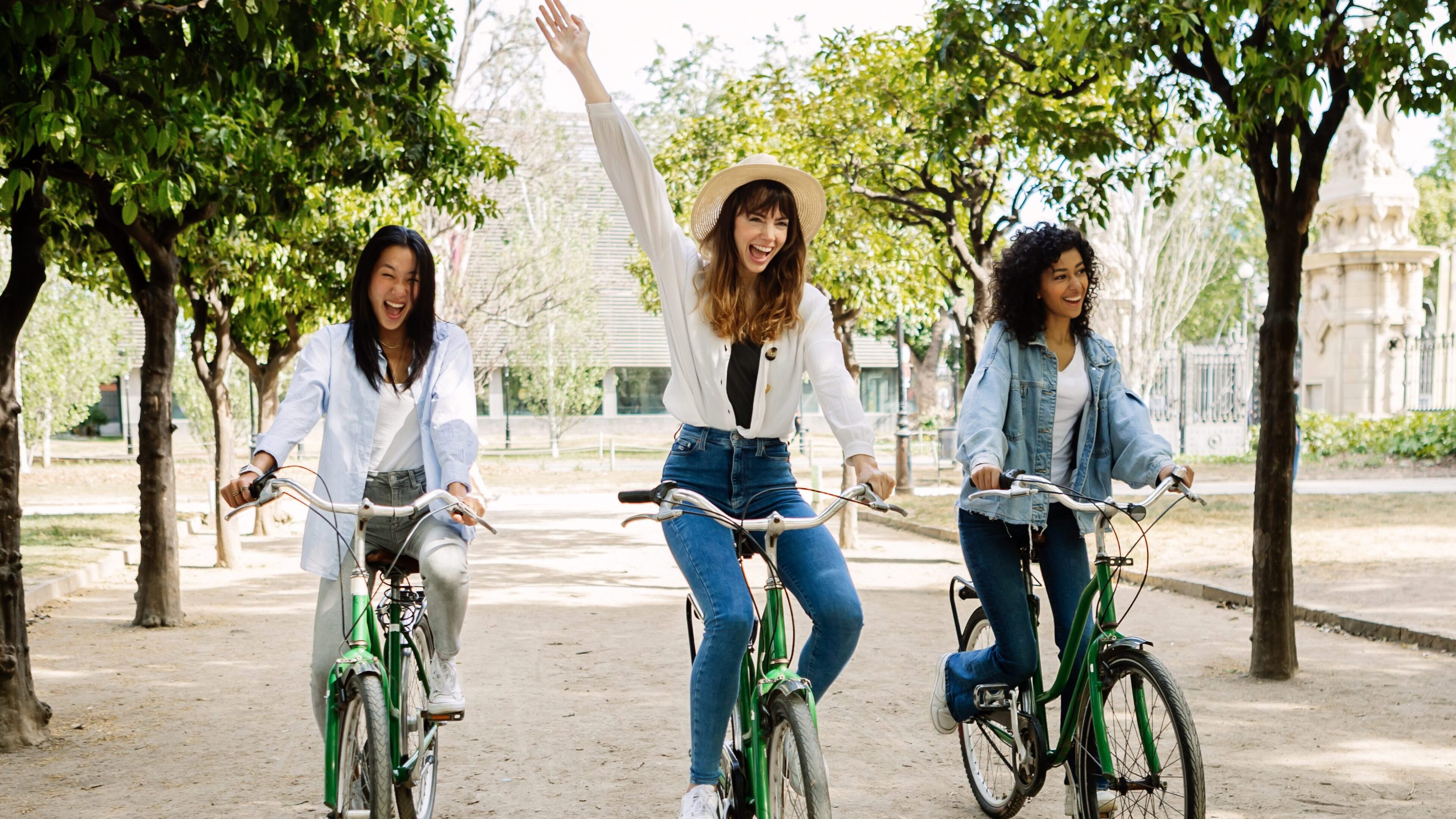 Three women riding bikes on a path in the park.